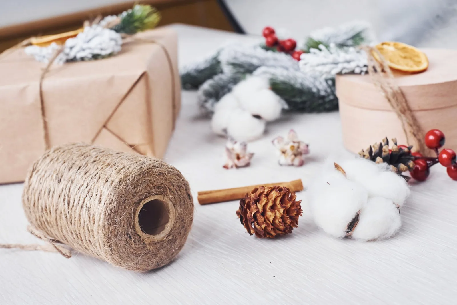 Twine spool, kraft-wrapped gifts, cotton bolls, pinecones, cinnamon stick, berries, and snow-dusted evergreen.